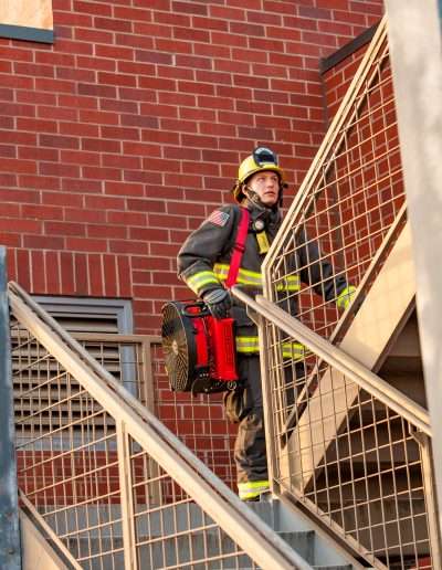 A firefighter walking up a staircase with the Squirt BlowHard fan model strapped over his right shoulder.